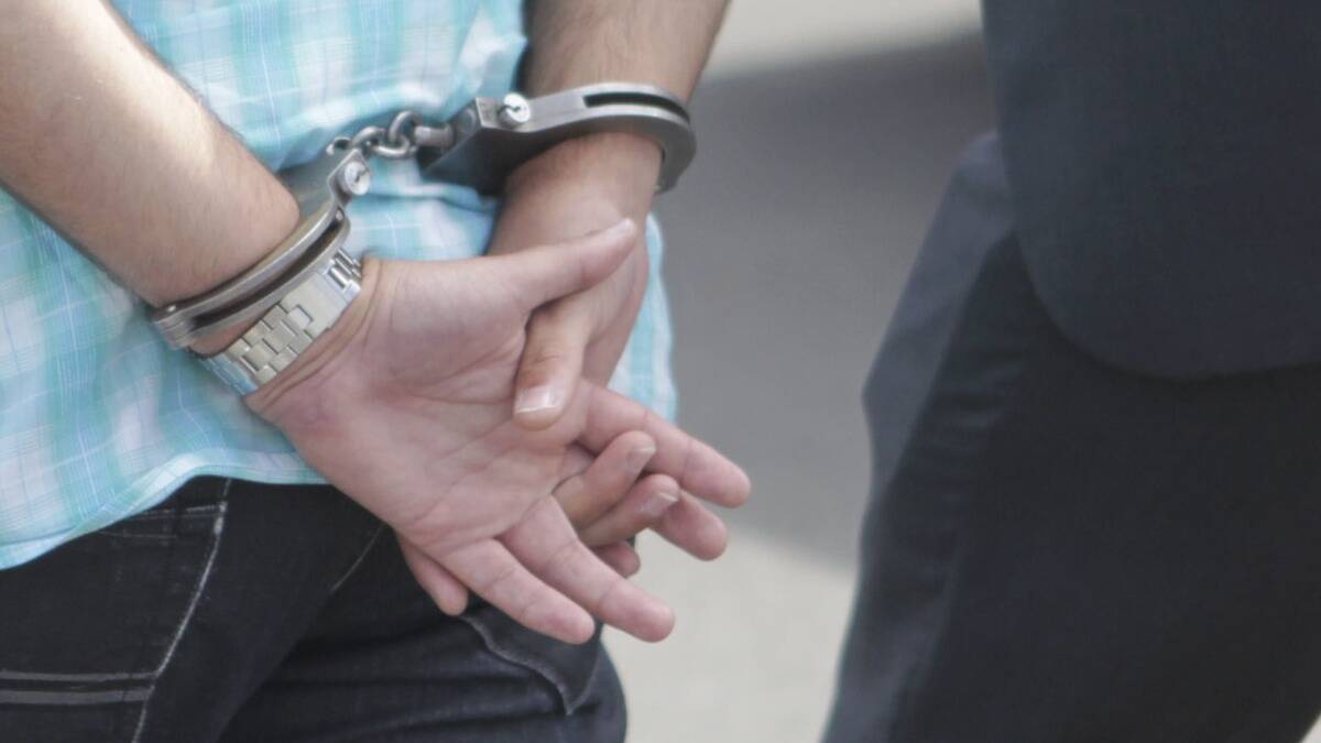 A person with their hands cuffed as they're escorted by an officer. File picture